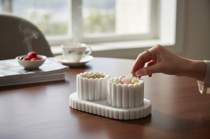 White marble fluted pinch pot set in use — hand reaching into cups filled with seeds and candy on dark wooden table