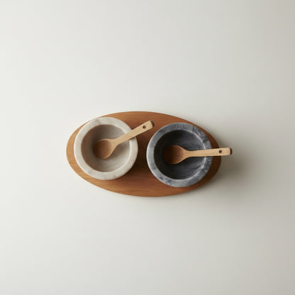 Selvada and Morchana marble pinch pot set — top-down view showing both contrasting cups with spoons on oval acacia tray