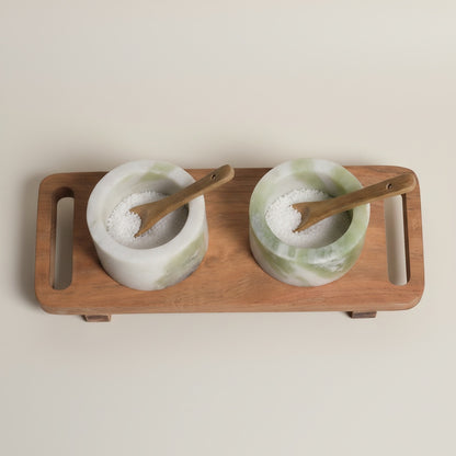Himalayan green marble pinch pot set — top-down view showing both cups filled with salt, wooden spoons resting inside, acacia tray below